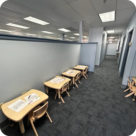 Row of small wooden tables and chairs set up along a hallway for children's activities.