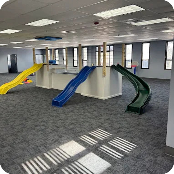 Indoor playroom featuring three slides in yellow, blue, and green.